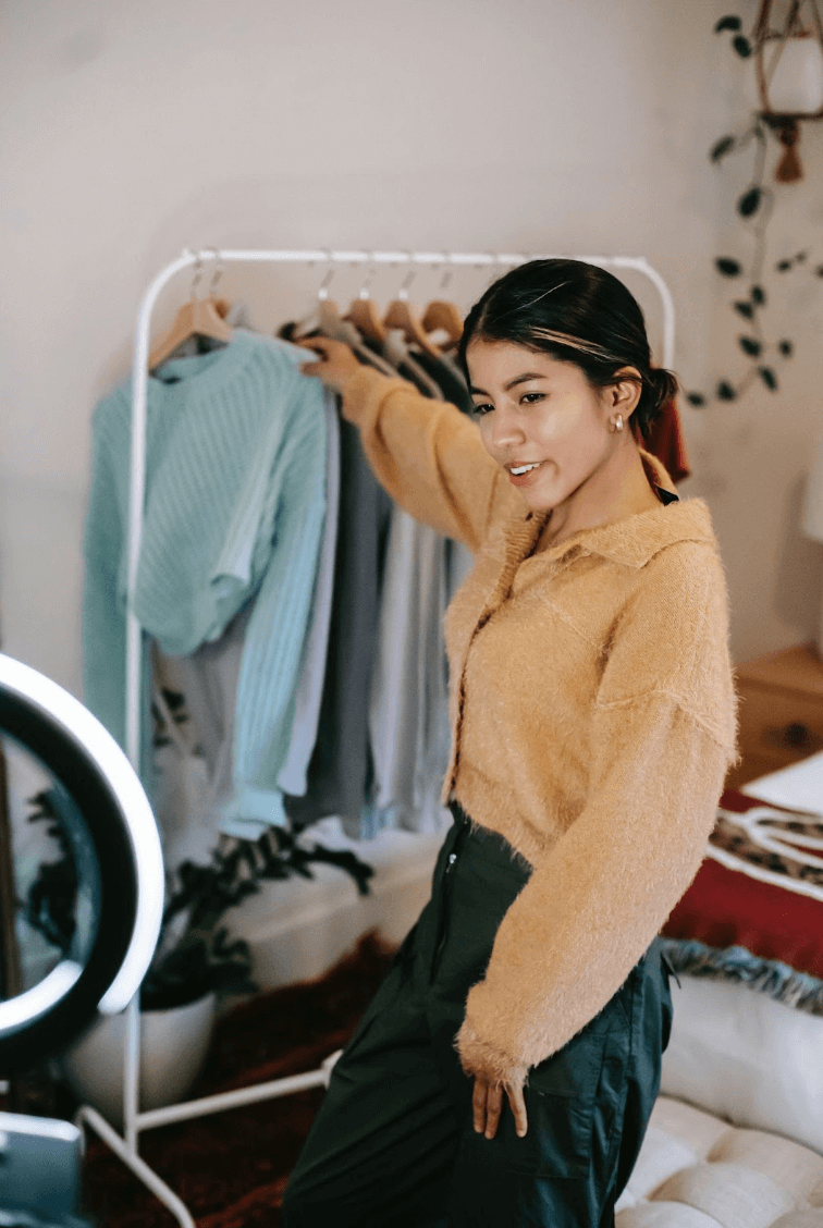 Trendy smiling woman taking clothes from rail while shooting video