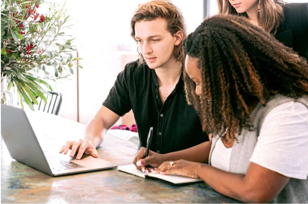 a man working on a laptop while a woman takes notes