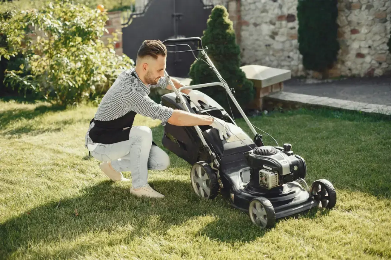 man-in-black-and-white-checkered-long-sleeve-shirt-and-denim-pants-sitting-beside-black-grass-cutter