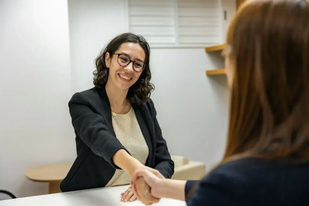 woman-shaking-hands-with-another-woman-sitting-at-a-table