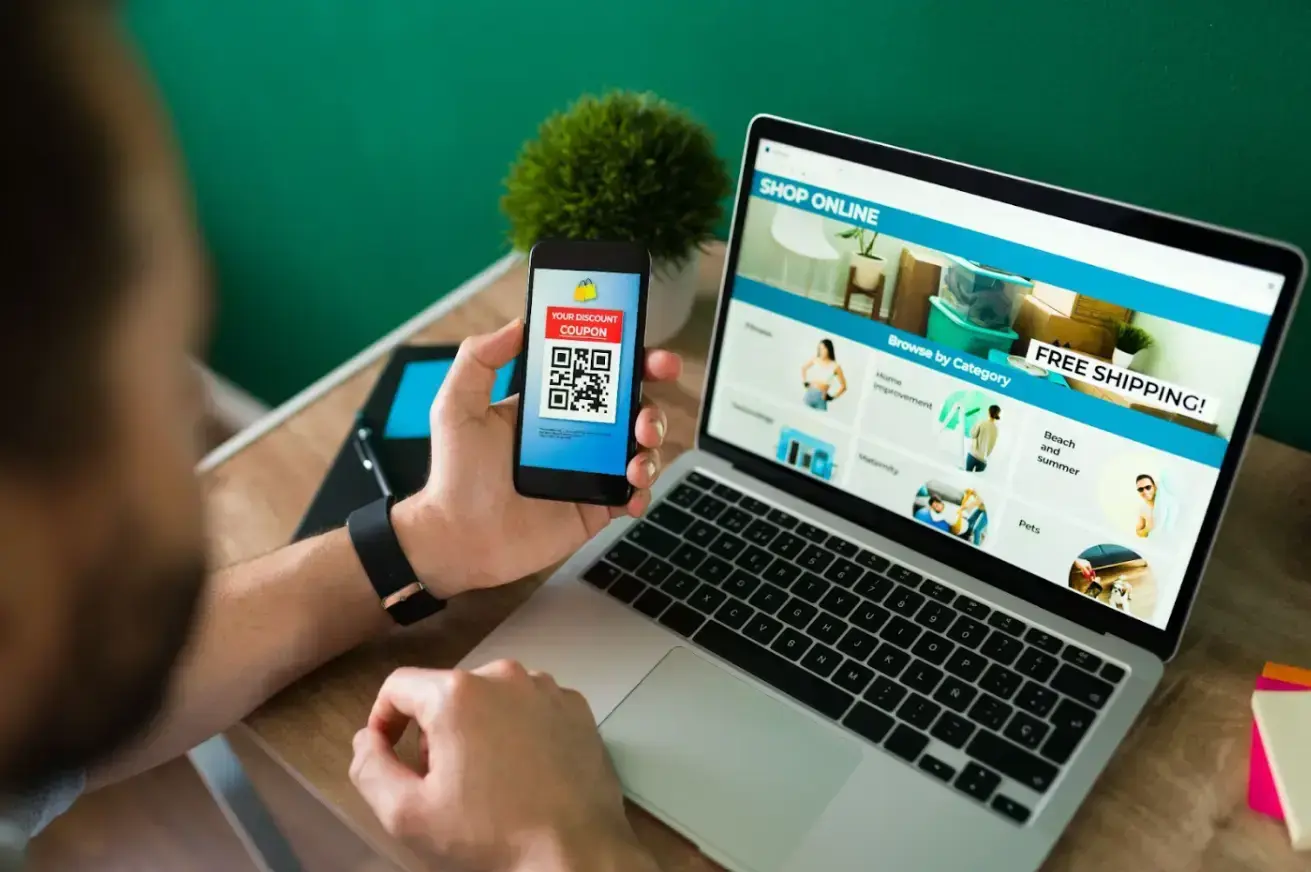 young-man-using-discount-coupon-his-smartphone-some-online-shopping-laptop